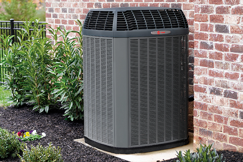 3 Tips to Prevent AC Breakdown During a Heat Wave. Photo of a black air conditioning unit installed outside of a brick home.